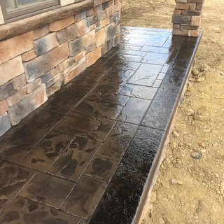 Wet dark stone walkway beside a brick house and porch over bare dirt