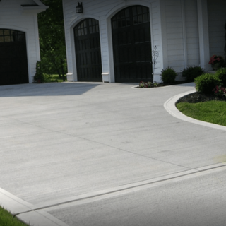 Concrete driveway in front of a white house with arched garage doors and a curved lawn edge