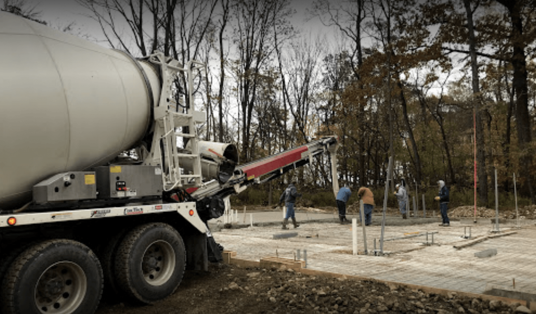 Concrete mixer truck pouring concrete at a wooded construction site with workers nearby