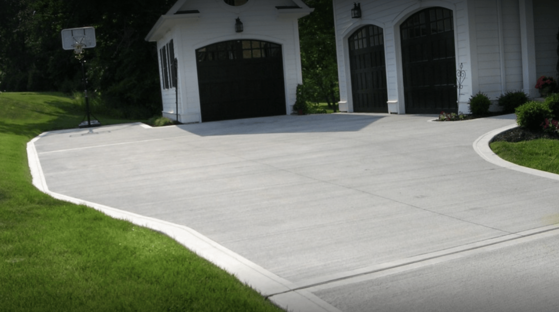 Concrete driveway leading to a white house with a garage, bordered by green lawn