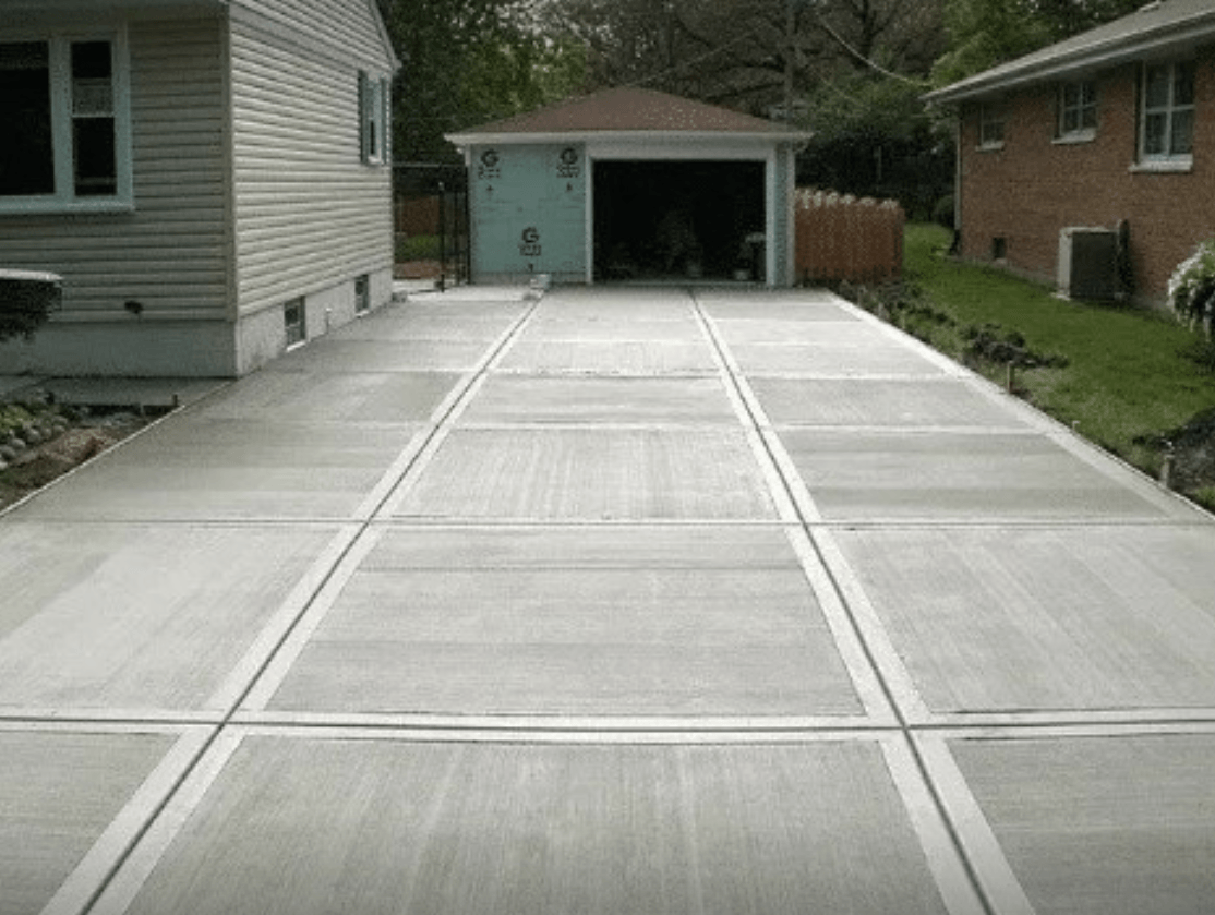 Concrete driveway leading to a detached garage between two houses, with a basketball hoop at the far end