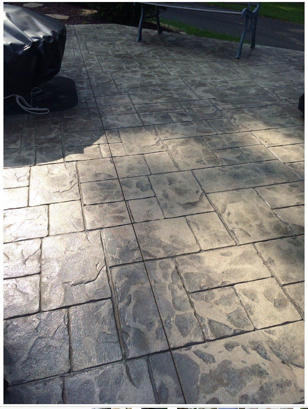 Sunlit stone-paved patio with a black vehicle at left and a bench in the background.